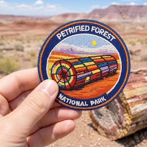 May include: A circular embroidered patch featuring a colorful petrified wood log in a desert landscape. The border is dark blue with the white text PETRIFIED FOREST NATIONAL PARK. The log displays vibrant red, yellow, blue, and purple segments.
