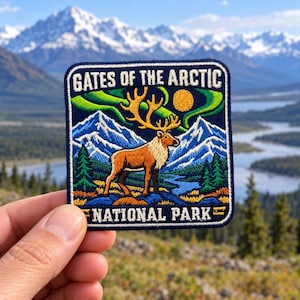May include: A square embroidered patch featuring a caribou standing in a landscape with mountains, pine trees, and a river. The sky displays a yellow sun and green aurora borealis. The text reads GATES OF THE ARCTIC NATIONAL PARK in white.