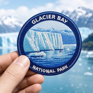 May include: A circular embroidered patch featuring a blue and white depiction of a glacier meeting the water. The text GLACIER BAY is arched at the top and NATIONAL PARK is arched at the bottom in white capital letters on a dark blue border.