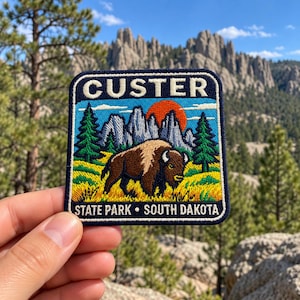 May include: A rectangular embroidered patch featuring a brown bison in a yellow field with green pine trees, grey mountain peaks, and a red sun. The text CUSTER is at the top, and STATE PARK • SOUTH DAKOTA is at the bottom in white letters.
