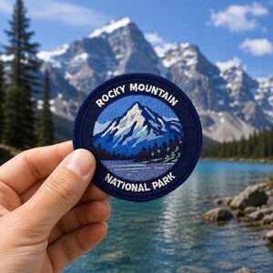 Può includere: Una toppa rotonda blu navy con un paesaggio montano e la scritta "Rocky Mountain National Park". Il design include una montagna innevata, un lago e alberi, in tonalità di blu e bianco.