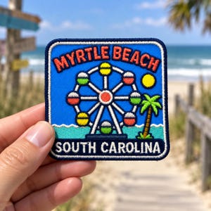 Peut inclure: Un écusson brodé carré sur fond bleu représentant une grande roue blanche, un palmier vert et un soleil jaune. Le texte MYRTLE BEACH est inscrit en orange en haut, et SOUTH CAROLINA est écrit en blanc dans la partie inférieure.