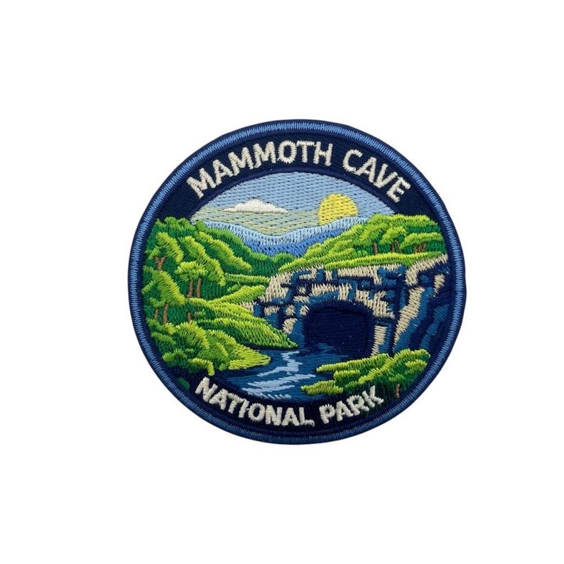 May include: Embroidered patch featuring a scenic view of Mammoth Cave National Park. The design includes a cave entrance, river, green trees, blue mountains, and a yellow sun. The text "Mammoth Cave National Park" is in a blue circular border.