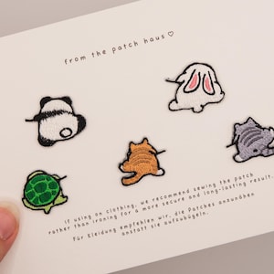 Op de afbeelding: Een witte kaart met geborduurde patches van een panda, konijn, kat, schildpad en nog een kat. De patches zijn in zwart, wit, oranje, grijs en groen. Bovenin staat de tekst "from the patch haus". De kaart bevat ook tekst over het naaien van patches.