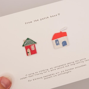 Könnte beinhalten: Zwei gestickte Hausaufnäher auf einer weißen Karte. Ein Haus ist rot mit grünem Dach, das andere ist weiß mit rotem Dach und blauem Fenster. Text: "from the patch haus" und Nähhinweise.