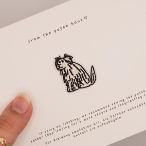 Könnte beinhalten: Gestickter Aufnäher mit einer stilisierten Hundeillustration in Schwarz-Weiß. Der Aufnäher befindet sich auf einer weißen Karte mit dem Text "from the patch haus" und Nähhinweisen.