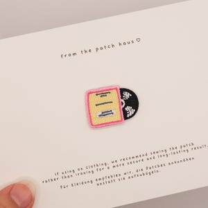 Könnte beinhalten: Ein gestickter Aufnäher in Form einer Schallplattenhülle, mit rosa Rand und schwarzer Schallplatte. Der Aufnäher befindet sich auf einer weißen Karte mit dem Text "from the patch haus" und Nähhinweisen.