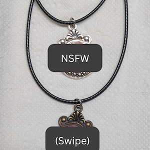 Puede incluir: Dos collares con colgantes decorativos. El colgante superior es plateado con un cordón negro. El colgante inferior es de color bronce con un cordón negro. La imagen incluye el texto "NSFW" y "(Swipe)".