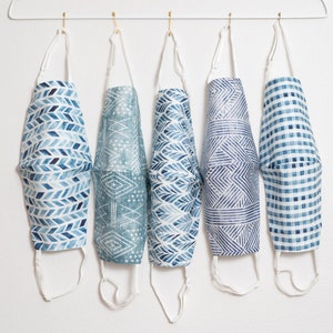 May include: Five blue and white patterned face masks hanging on a white hanger. The masks have different geometric designs.