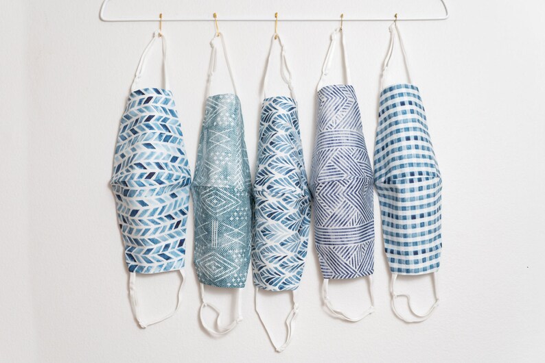 May include: Five blue and white patterned face masks hanging on a white hanger. The masks have different geometric designs.