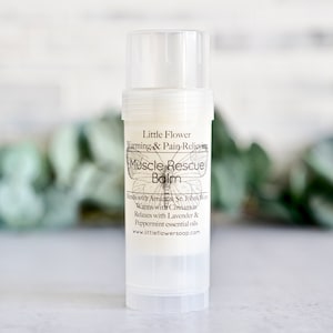 May include: A white tube of Little Flower Warming & Pain-Relieving Muscle Rescue Balm. The label features a butterfly design and lists the ingredients: Arnica, St. John's Wort, Cinnamon, Lavender, and Peppermint essential oils. The website address is www.littleflowersoap.com.