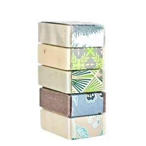 May include: A stack of five bars of soap with different patterned paper wrappers. The wrappers feature green, blue, and white floral designs.