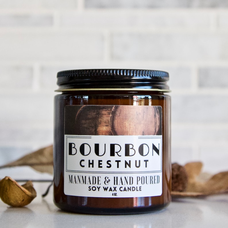 Puede incluir: Una vela de vidrio marr&oacute;n con tapa negra y una etiqueta blanca que dice "Bourbon Chestnut" y "Handmade & Hand Poured Soy Wax Candle 4 oz."