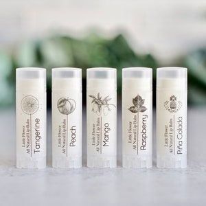 May include: Five lip balm tubes with white labels and clear caps. Each tube features a different fruit illustration: tangerine, peach, mango, raspberry, and pi&ntilde;a colada. The text "Little Flower All Natural Lip Balm" is printed on each tube.