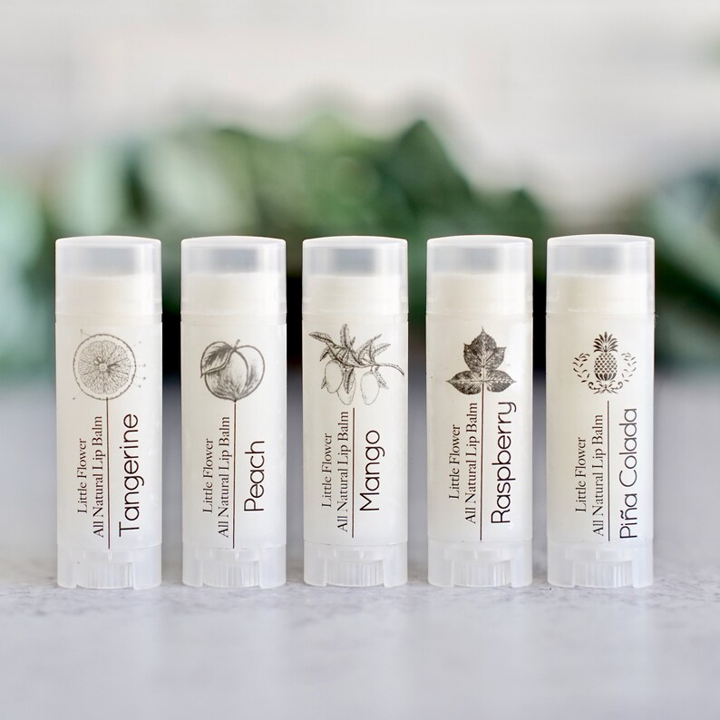 May include: Five lip balm tubes with white labels and clear caps. Each tube features a different fruit illustration: tangerine, peach, mango, raspberry, and pi&ntilde;a colada. The text "Little Flower All Natural Lip Balm" is printed on each tube.