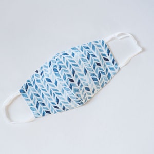 May include: A white face mask with blue and white geometric pattern. The mask has white elastic straps.