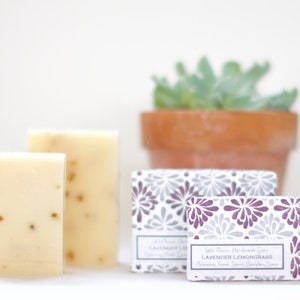 May include: Two bars of white soap with a light green fleck, packaged in a white box with a purple and gray floral design. The box has the text "Lavender Lemongrass" printed on it.