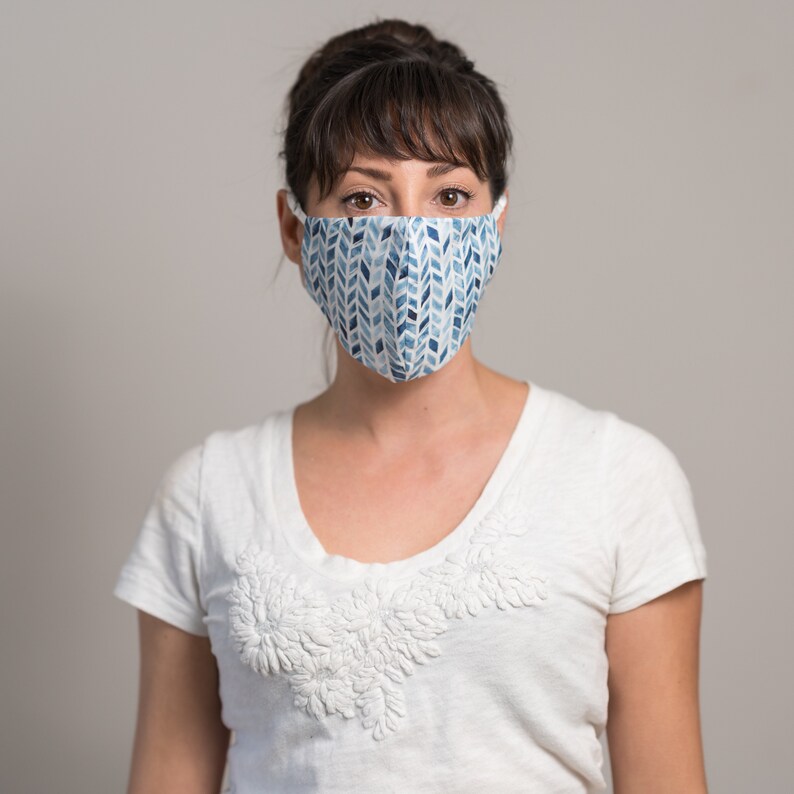 May include: A woman wearing a white t-shirt with a blue and white patterned face mask.