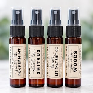 May include: Four amber glass spray bottles with black caps and beige labels. The labels feature black text including the phrases: Smells like POOPERMINT, Smells like SHITRUS, LET THAT SHIT GO, and Shit in the WOODS, along with other descriptive text.