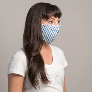May include: A woman with long brown hair is wearing a white t-shirt and a blue and white checkered face mask.