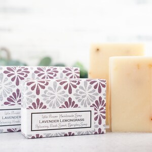 May include: Two bars of handmade soap in boxes with floral patterns. The soap is white with dried herbs and the boxes have the text "Little Flower Handmade Soap Lavender Lemongrass Relaxing, Fresh Scent, Everyday Soap" and "Little Flower Lavender Relaxing, Fresh".