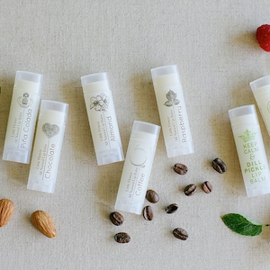 May include: A collection of ten different flavored lip balms in white tubes with black text and illustrations. The flavors include Peppermint, Piña Colada, Chocolate, Coffee, Almond, Vanilla, Raspberry, Tangerine, and Keep Calm & Dill Pickle.