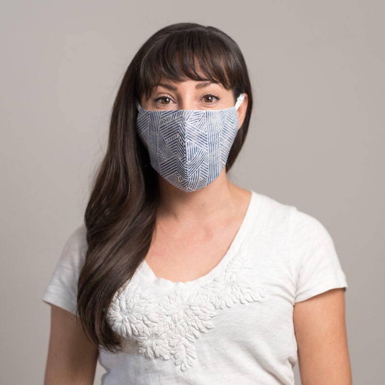 May include: A woman wearing a white shirt with a blue and white patterned face mask.