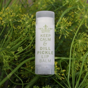 May include: A white tube of lip balm with a green label that says "Keep Calm & Dill Pickle Lip Balm". The tube is surrounded by green dill plants.