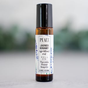 May include: A small brown glass bottle with a black roll-on top. The label is white with black text that reads "PEACE LAVENDER BERGAMOT essential oil ROLL ON The Little Flower Soap Co 0.350Z / 10.35ML".