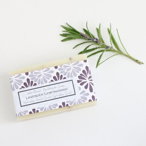 May include: A white bar of soap with a purple and white floral pattern on the label. The label reads "Little Flower Handmade Soap Lavender Lemongrass Relaxing, Fresh Scent, Everyday Soap".
