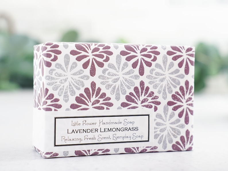 May include: A white box with a purple and silver floral pattern. The box contains a bar of lavender lemongrass soap. The label reads "Little Flower Handmade Soap Lavender Lemongrass Relaxing, Fresh Scent, Everyday Soap".