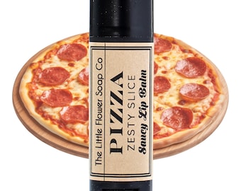 Puede incluir: Un tubo negro de bálsamo labial con una etiqueta marrón que dice "The Little Flower Soap Co. Pizza Zesty Slice Saucy Lip Balm". El bálsamo labial está delante de una pizza de pepperoni sobre una tabla de cortar de madera.