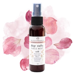 May include: A brown glass bottle of Rose Water Face Mist with a black spray nozzle. The label reads "Refresh & Hydrate" and lists ingredients. The background features pink watercolor and rose petals. The bottle contains 2 fl oz.