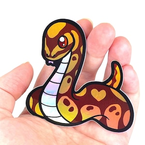 May include: A sticker of a cartoon snake with a brown, orange, and yellow iridescent pattern. The snake has a heart-shaped pattern on its tail.