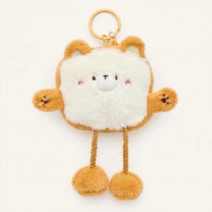 May include: A plush bear keychain featuring a square-shaped white face with brown ears and limbs. The bear has embroidered facial features, pink cheeks, and small brown paw prints on its hands. It is attached to a gold-toned metal ring.