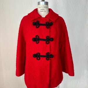 May include: A vibrant red coat with a classic design. The coat features a collar and three black frog closures. The coat is displayed on a mannequin. The text "SUPERIOR MODEL FORM CO" is visible on the mannequin.