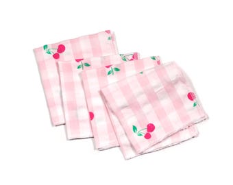 Op de afbeelding: Vier roze en witte gingham stoffen servetten met een kersenprint.
