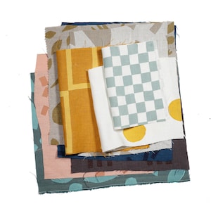 May include: A stack of fabric swatches in various colours and patterns, including yellow, blue, and brown. The fabrics are arranged in a layered fashion, with the top layer being a yellow fabric with a geometric pattern.