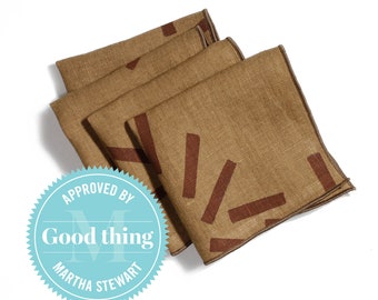 Pode incluir: Conjunto de quatro guardanapos de linho castanho com um padrão geométrico castanho. Os guardanapos estão dobrados e empilhados. A imagem inclui um selo de aprovação Martha Stewart Good Thing.