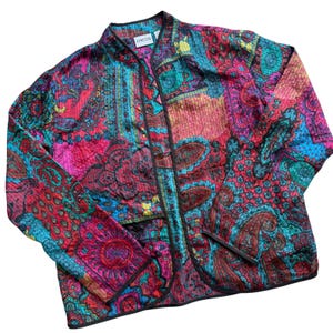 May include: A long-sleeve jacket by Chico's featuring a vibrant, multi-colored paisley and geometric pattern in shades of magenta, teal, and black. The jacket has a mandarin collar, a front button closure, and black piping along the edges.