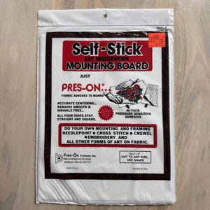 Könnte beinhalten: Versiegelte Verpackung mit einer selbstklebenden Art Needlework Mounting Board. Die Tafel ist weiß mit einem dunkelbraunen Rand und hat roten und schwarzen Text. Die Verpackung enthält den Text "Pres-On" und "Hochleistungs-Druckklebstoff".