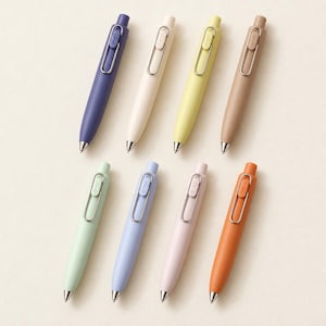 Könnte beinhalten: Ein Set aus acht einziehbaren Kugelschreibern in verschiedenen matten Pastell- und gedeckten Farben, darunter Dunkelblau, Creme, Gelb, Beige, Hellgrün, Hellblau, Rosa und Orange, jeweils mit silbernem Metallclip und Spitze.