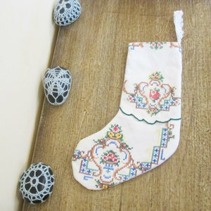 May include: White Christmas stocking with a green scalloped edge and embroidered floral design in shades of red, green, blue, and yellow.