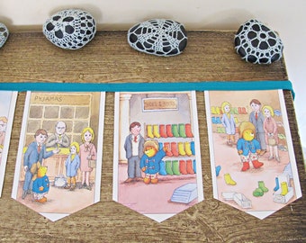 May include: A colorful banner with three illustrations of a bear shopping for pajamas, shoes and boots. The banner is made of paper and has a teal ribbon running through it.