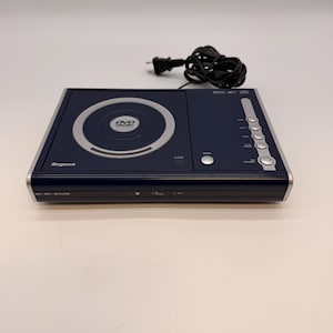 May include: A dark blue Regent DVD/MP3/CD player with a silver trim. The player has a circular disc tray and a series of silver buttons on the right side. A black power cord is connected to the player.