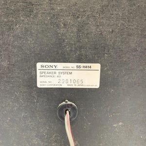 May include: A black Sony speaker system, model number SS-H414, with an impedance of 6 ohms. The label includes the serial number 2981065 and states it was made in Japan. A two-wire speaker cable extends from a circular port below the label.