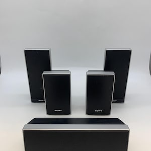 May include: A set of five black and silver Sony speakers. The collection includes one horizontal center speaker and four vertical satellite speakers, each featuring a black mesh front grille with the Sony logo printed in white at the bottom.