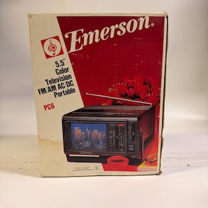K&ouml;nnte beinhalten: Ein Vintage Emerson 5,5" Farbfernseher, FM/AM AC/DC tragbar, Modell PC6, in der Originalverpackung. Die Box hat ein rot-wei&szlig;es Design mit dem Emerson-Logo und einer Grafik des Fernsehers. Der Fernseher zeigt eine Stadtlandschaft.