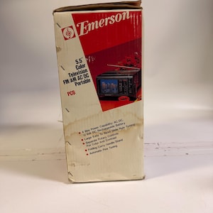 K&ouml;nnte beinhalten: Eine Emerson PC6 tragbare Farbfernsehbox. Die Box ist cremefarben mit einem roten Diagonalstreifen und dem Emerson-Logo. Sie verf&uuml;gt &uuml;ber einen 14 cm Farbfernseher, FM/AM-Radio und AC/DC-Stromversorgung. Mit klappbarem Tragegriff und automatischer Feinabstimmung.