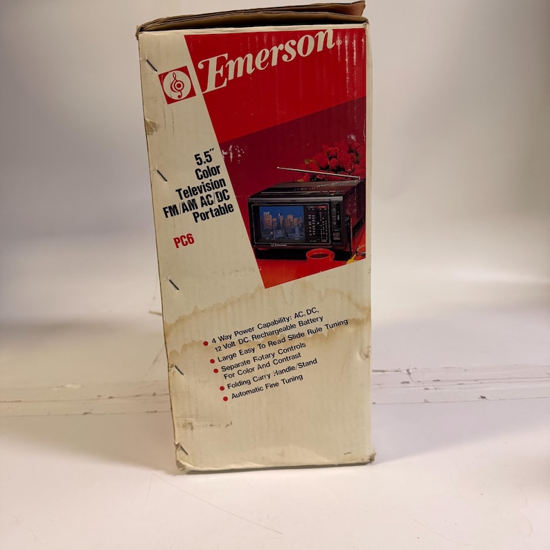 K&ouml;nnte beinhalten: Eine Emerson PC6 tragbare Farbfernsehbox. Die Box ist cremefarben mit einem roten Diagonalstreifen und dem Emerson-Logo. Sie verf&uuml;gt &uuml;ber einen 14 cm Farbfernseher, FM/AM-Radio und AC/DC-Stromversorgung. Mit klappbarem Tragegriff und automatischer Feinabstimmung.